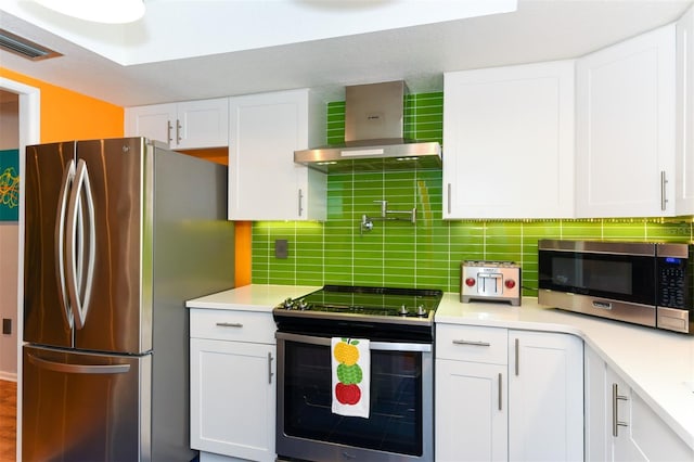 kitchen featuring wall chimney exhaust hood, decorative backsplash, white cabinetry, and stainless steel appliances