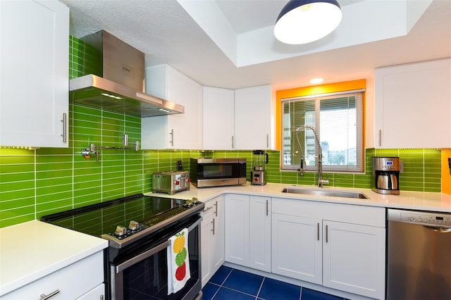 kitchen featuring wall chimney exhaust hood, sink, appliances with stainless steel finishes, and white cabinets