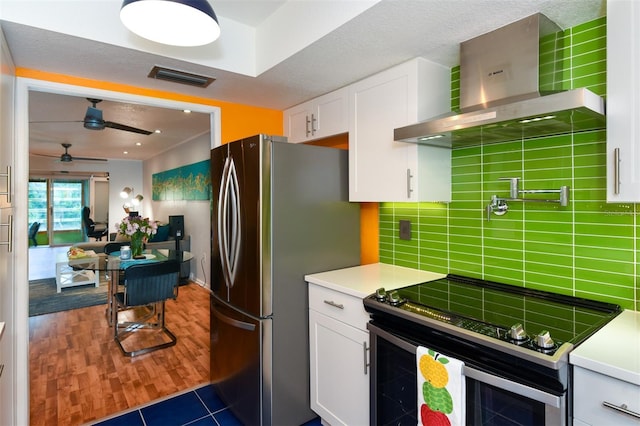 kitchen featuring electric range oven, wall chimney exhaust hood, decorative backsplash, and white cabinets