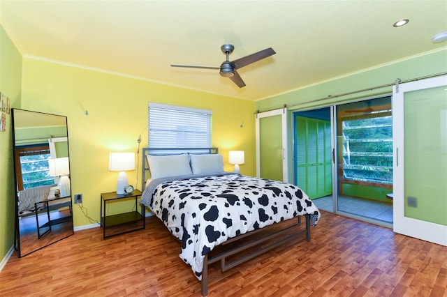 bedroom featuring crown molding, a barn door, wood-type flooring, and ceiling fan