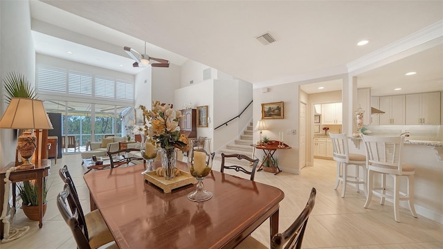 dining room featuring a high ceiling, a ceiling fan, visible vents, stairs, and baseboards