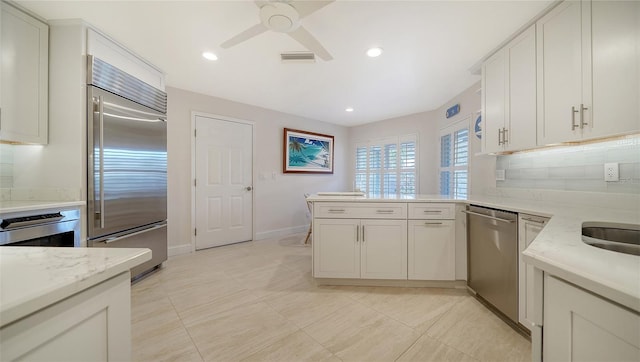 kitchen with appliances with stainless steel finishes, white cabinets, decorative backsplash, and light stone countertops