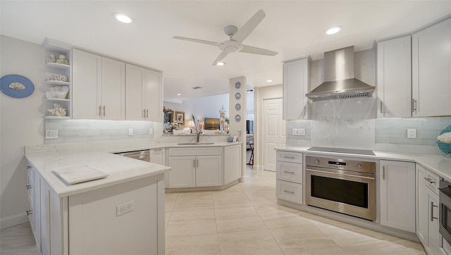 kitchen featuring tasteful backsplash, appliances with stainless steel finishes, wall chimney range hood, a sink, and a peninsula