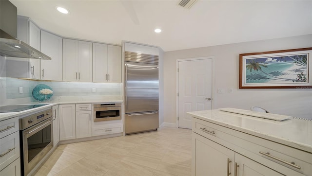 kitchen featuring appliances with stainless steel finishes, light stone countertops, wall chimney range hood, and backsplash