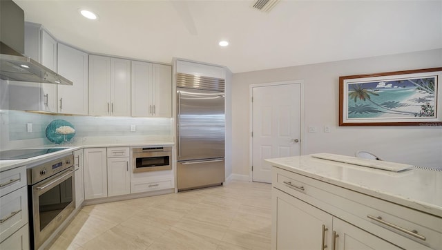 kitchen with tasteful backsplash, wall chimney exhaust hood, appliances with stainless steel finishes, and light stone countertops