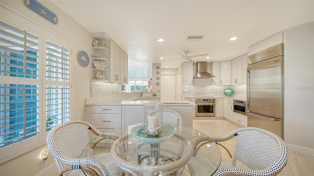 kitchen featuring backsplash, stainless steel appliances, wall chimney range hood, and white cabinets