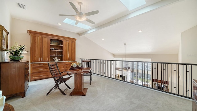 home office featuring light carpet, vaulted ceiling with skylight, and ceiling fan