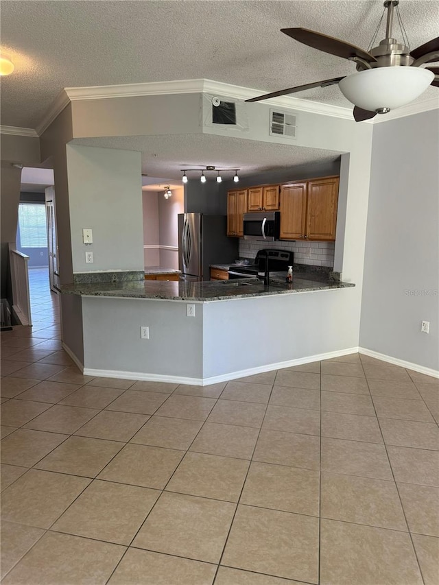 kitchen with kitchen peninsula, appliances with stainless steel finishes, a textured ceiling, dark stone countertops, and light tile patterned flooring