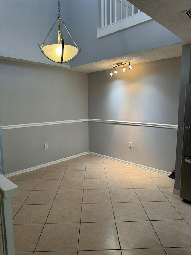 tiled empty room featuring track lighting and a textured ceiling