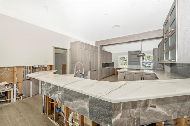 kitchen with kitchen peninsula, light stone counters, pendant lighting, light hardwood / wood-style floors, and a breakfast bar area