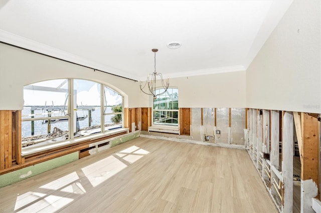 unfurnished dining area featuring a notable chandelier, crown molding, wooden walls, a water view, and light wood-type flooring