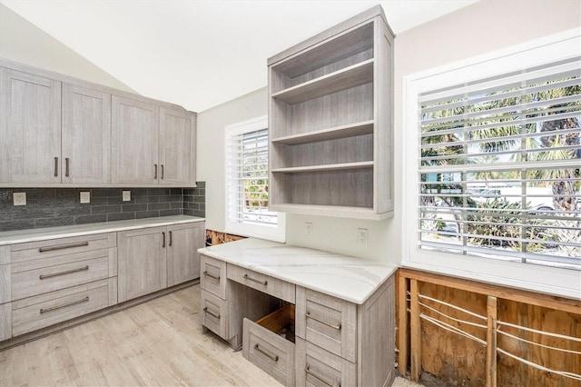 kitchen featuring light stone countertops, backsplash, light hardwood / wood-style floors, and vaulted ceiling