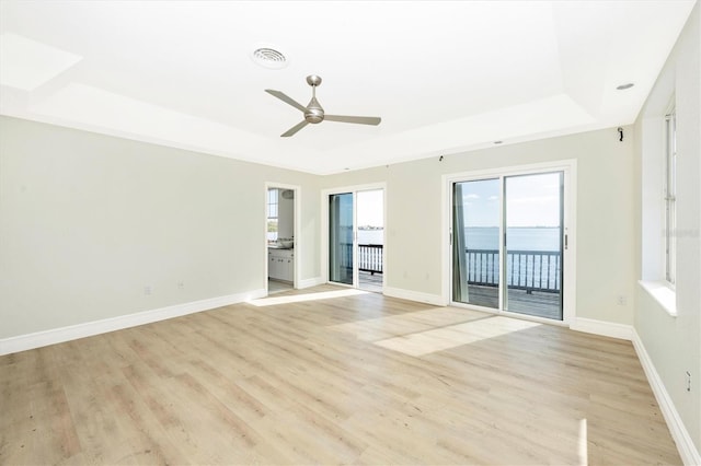 spare room featuring light hardwood / wood-style floors, a raised ceiling, ceiling fan, and a water view