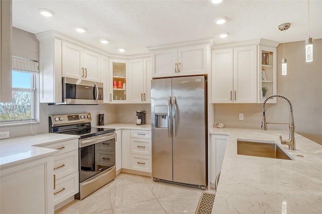 kitchen with white cabinets, light stone counters, stainless steel appliances, sink, and decorative light fixtures