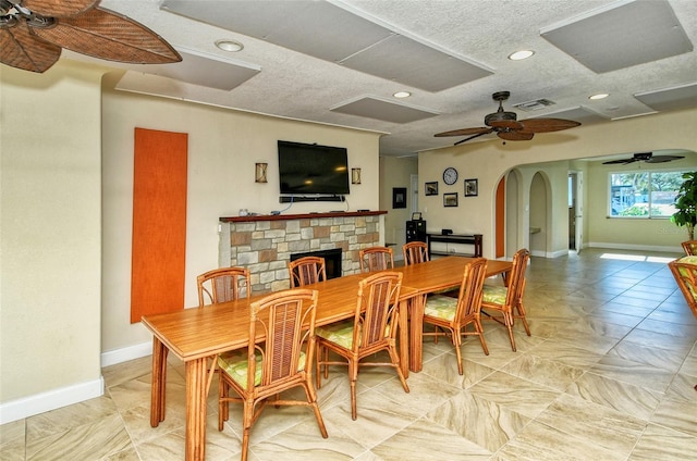 dining area featuring a stone fireplace, a textured ceiling, and ceiling fan