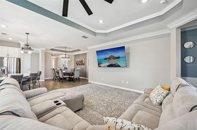 living room with a tray ceiling, ornamental molding, dark hardwood / wood-style flooring, and ceiling fan with notable chandelier