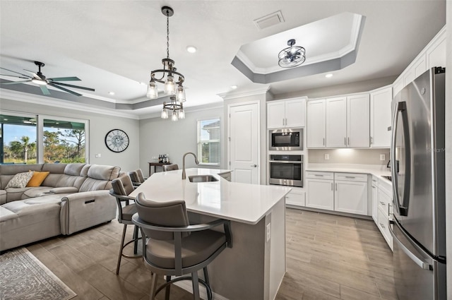 kitchen with sink, a tray ceiling, white cabinetry, stainless steel appliances, and decorative light fixtures