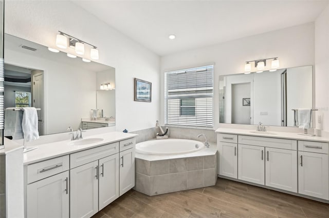 bathroom featuring vanity, a relaxing tiled tub, hardwood / wood-style flooring, and a wealth of natural light