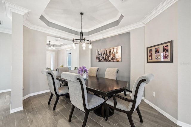 dining room with hardwood / wood-style flooring, a notable chandelier, ornamental molding, and a tray ceiling