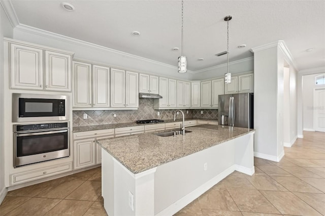 kitchen with tasteful backsplash, sink, stainless steel appliances, light stone counters, and a center island with sink