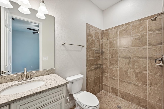 bathroom featuring toilet, ceiling fan, vanity, and tiled shower