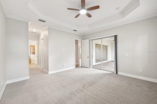 unfurnished bedroom featuring ceiling fan, a raised ceiling, crown molding, a closet, and light colored carpet