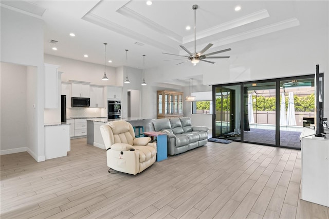 living room with light hardwood / wood-style flooring, a raised ceiling, and ceiling fan