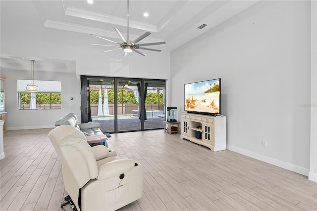 living room featuring a towering ceiling, light wood-type flooring, a tray ceiling, ceiling fan, and crown molding