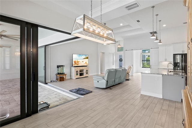 living room with a raised ceiling, ceiling fan, a barn door, a high ceiling, and light hardwood / wood-style floors