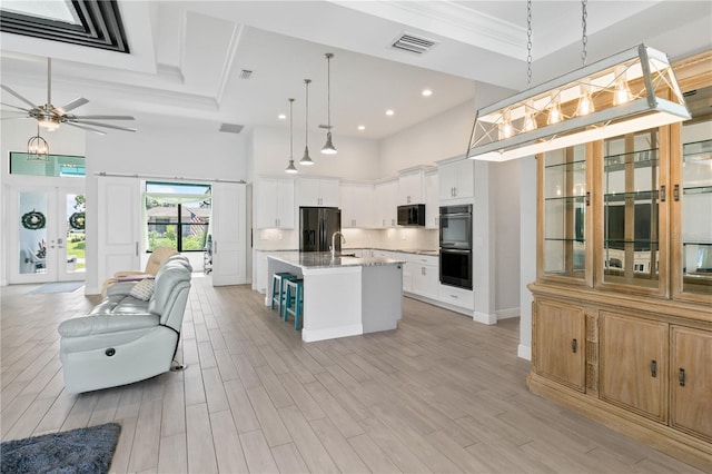 kitchen with white cabinets, an island with sink, black appliances, a high ceiling, and decorative light fixtures