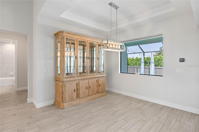 unfurnished dining area featuring a raised ceiling, ornamental molding, and light hardwood / wood-style flooring