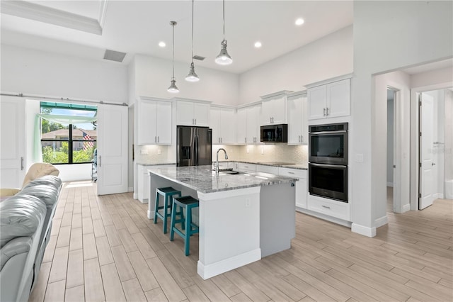 kitchen with white cabinetry, black appliances, a high ceiling, and an island with sink