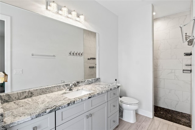 bathroom featuring a tile shower, hardwood / wood-style flooring, vanity, and toilet