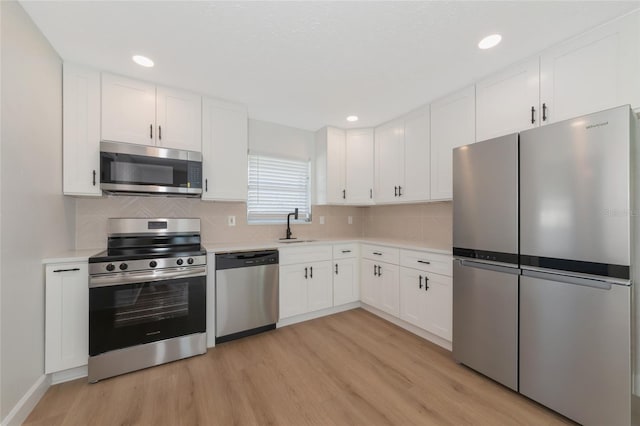 kitchen with white cabinets, decorative backsplash, appliances with stainless steel finishes, light hardwood / wood-style flooring, and sink