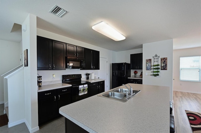 kitchen featuring black appliances, sink, an island with sink, a kitchen breakfast bar, and light hardwood / wood-style floors