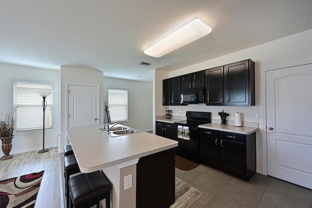 kitchen featuring black appliances, a textured ceiling, sink, a kitchen island with sink, and a breakfast bar