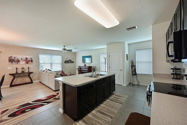 kitchen with a textured ceiling, sink, dishwasher, ceiling fan, and a kitchen island with sink