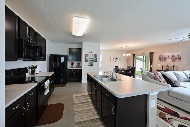 kitchen with black appliances, sink, light tile patterned floors, a kitchen island with sink, and decorative light fixtures