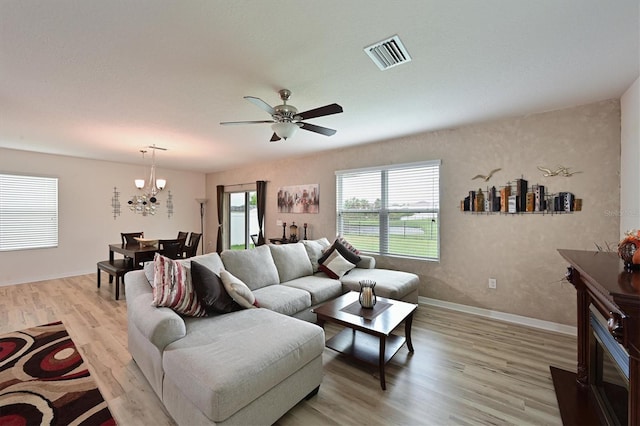 living room with ceiling fan with notable chandelier and light hardwood / wood-style flooring