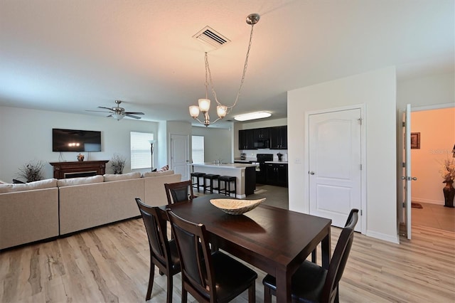 dining space with ceiling fan with notable chandelier and light hardwood / wood-style floors