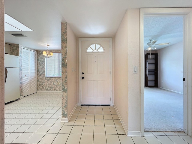 tiled entryway with a textured ceiling and ceiling fan with notable chandelier