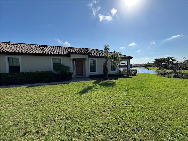 view of front facade with a water view, stucco siding, a tiled roof, and a front yard