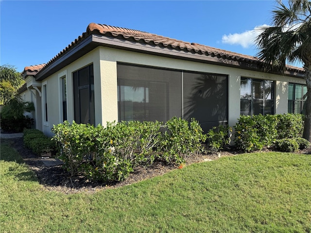 view of property exterior with stucco siding, a tile roof, a sunroom, and a yard