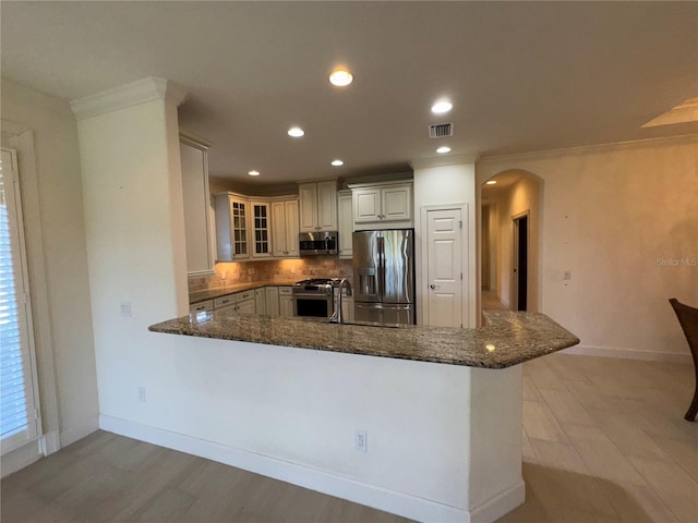 kitchen featuring arched walkways, stainless steel appliances, a peninsula, decorative backsplash, and glass insert cabinets