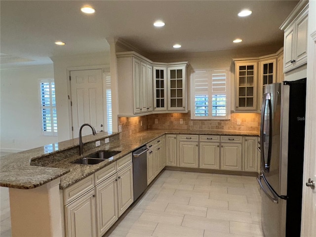 kitchen featuring stone counters, backsplash, appliances with stainless steel finishes, a sink, and a peninsula