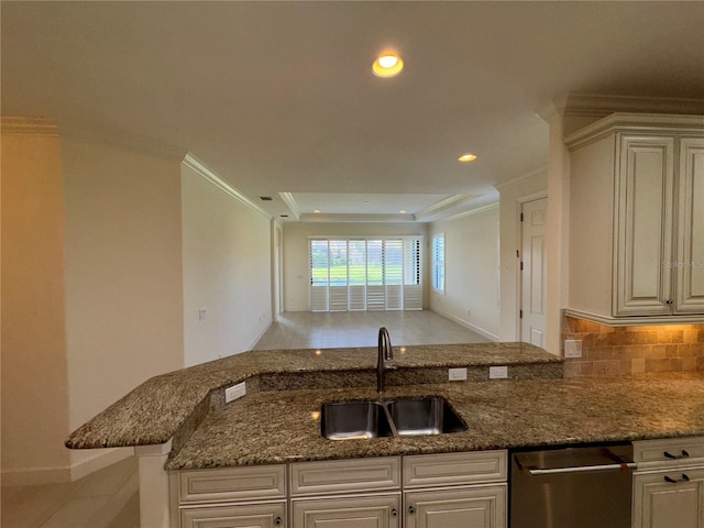 kitchen with a peninsula, a sink, ornamental molding, stainless steel dishwasher, and dark stone countertops