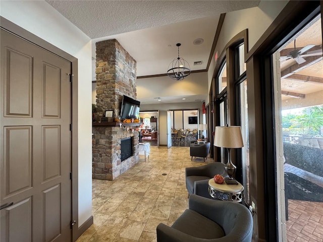 living area with a notable chandelier, visible vents, a stone fireplace, a textured ceiling, and baseboards