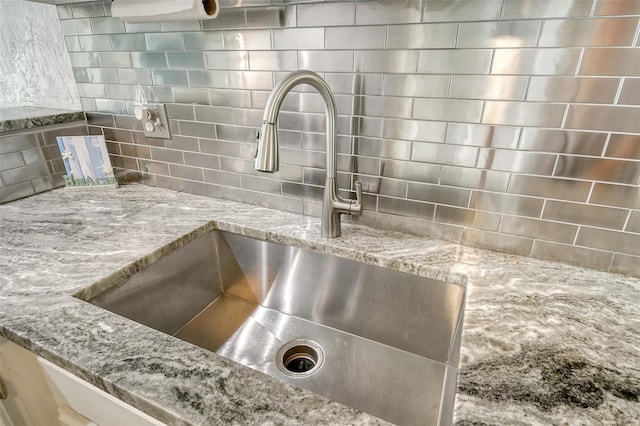 room details featuring decorative backsplash, light stone countertops, and sink