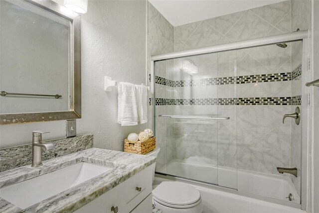 full bathroom featuring toilet, combined bath / shower with glass door, and vanity