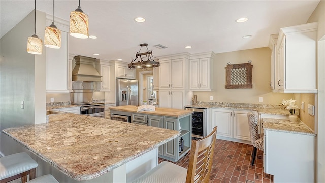 kitchen with a center island, decorative light fixtures, white cabinets, custom range hood, and appliances with stainless steel finishes